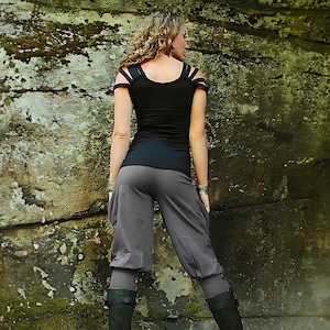 Może przedstawiać: Kobieta w czarnym topie z wyciętymi ramiączkami i szarych spodniach. Ma na sobie czarne buty i związane włosy.