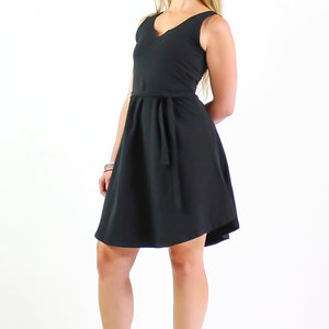 May include: A black sleeveless dress with a V-neckline and a tie belt. The dress has a flowy skirt and is worn with brown platform clogs.