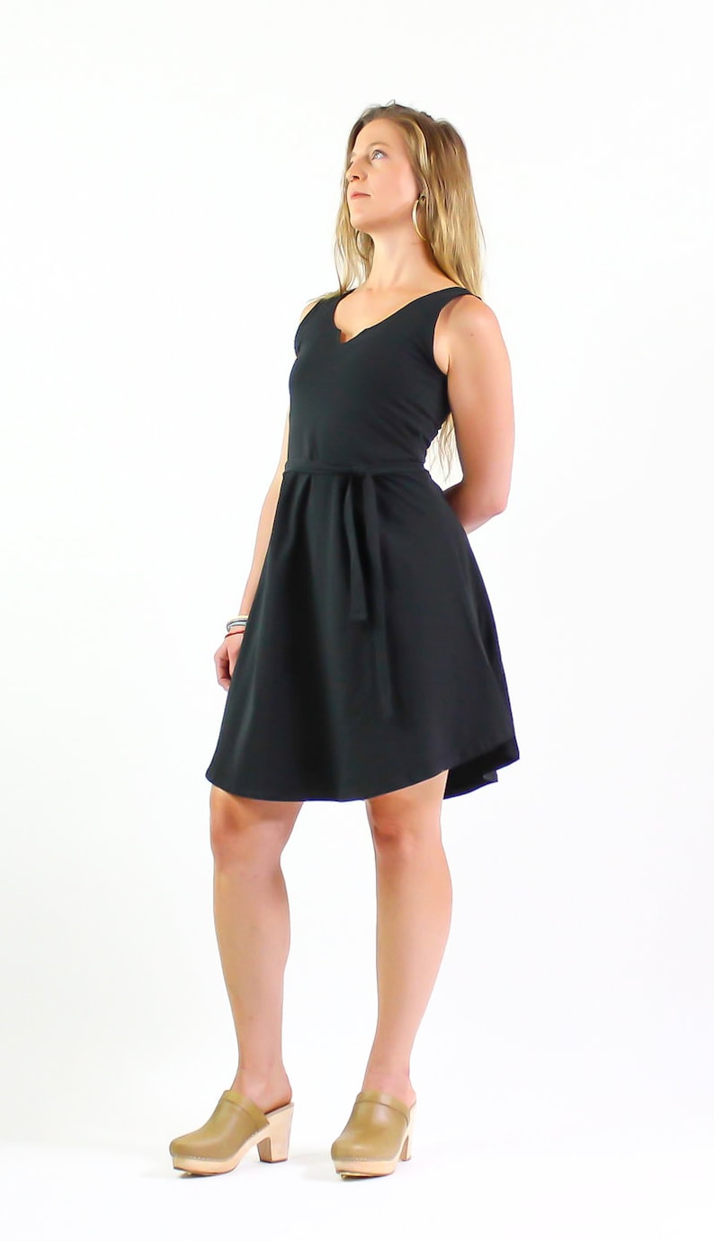 May include: A black sleeveless dress with a V-neckline and a tie belt. The dress has a flowy skirt and is worn with brown platform clogs.