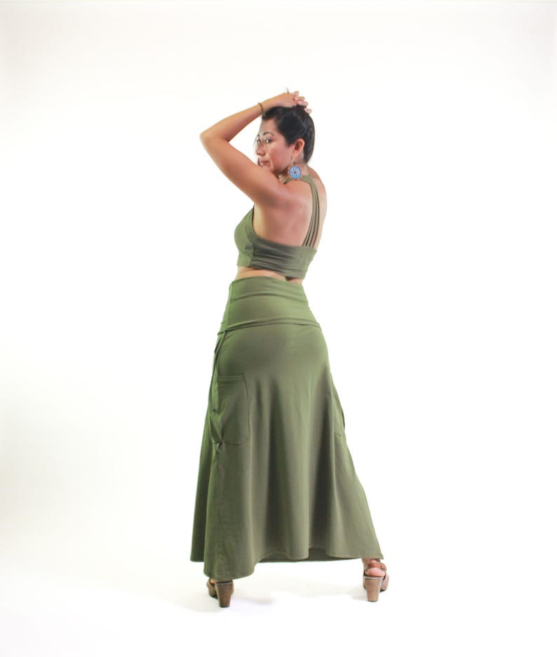 May include: A woman wearing a green crop top and a long, flowing green skirt with a pocket. The skirt is gathered at the waist and has a flowing, A-line shape.