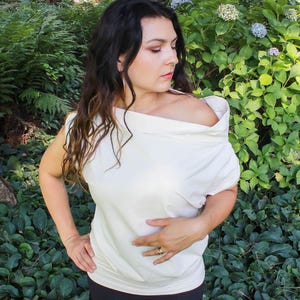 May include: A white off-the-shoulder top with a draped neckline. The top is made of a soft, lightweight fabric and has a relaxed fit.