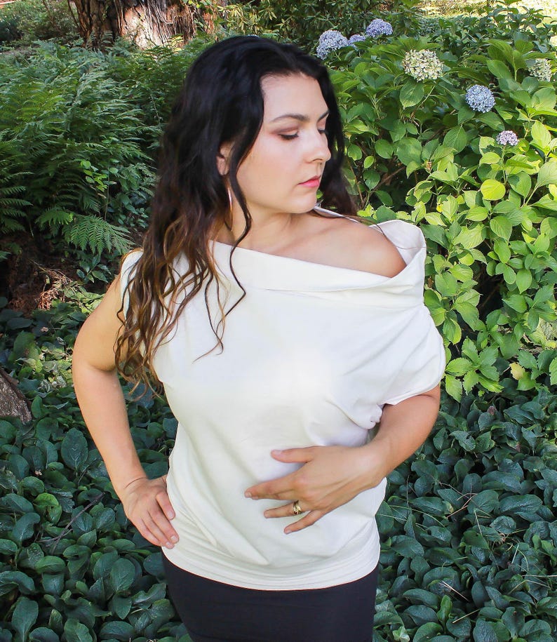 May include: A white off-the-shoulder top with a draped neckline. The top is made of a soft, lightweight fabric and has a relaxed fit.