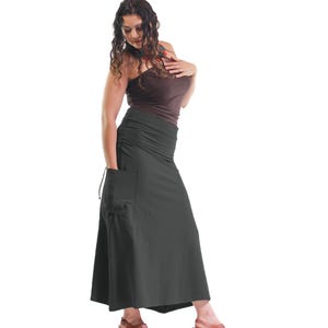 May include: A woman wearing a brown tank top and a long, dark gray skirt with a large pocket on the left side. She is wearing brown heeled sandals.
