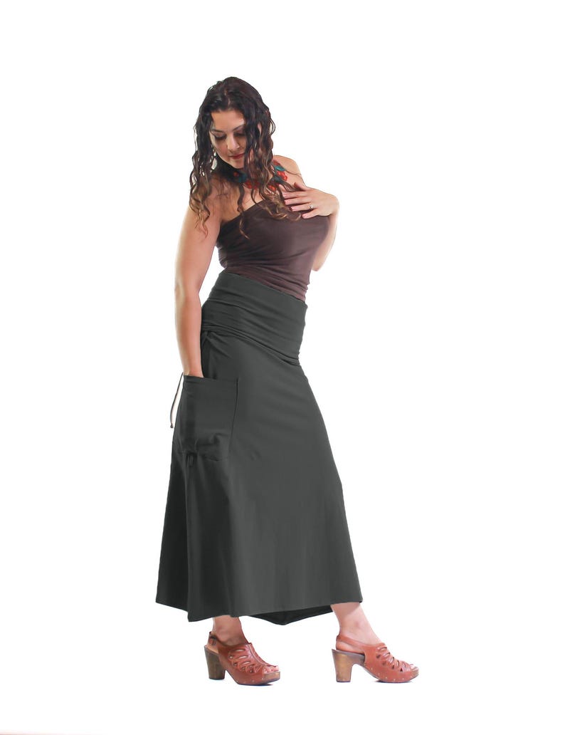 May include: A woman wearing a brown tank top and a long, dark gray skirt with a large pocket on the left side. She is wearing brown heeled sandals.