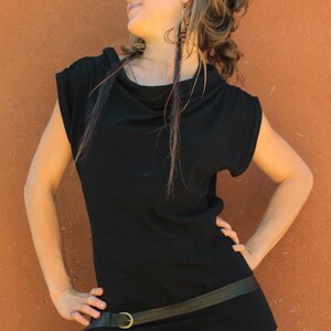 May include: A black cowl neck top with a black leather belt and a brass buckle. The model is wearing burgundy leggings.