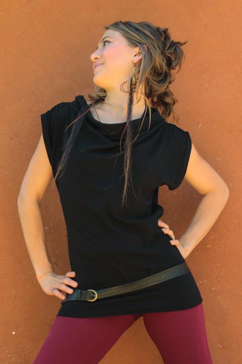 May include: A black cowl neck top with a black leather belt and a brass buckle. The model is wearing burgundy leggings.