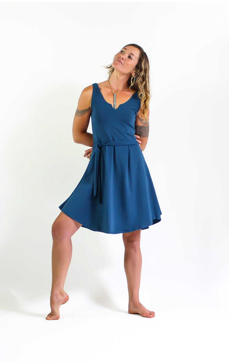 May include: A woman wearing a teal blue sleeveless dress with a tie belt. The dress has a V-neckline and a flowy skirt.