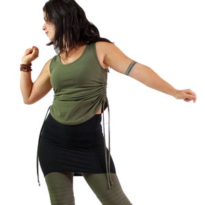 May include: A woman wearing a green tank top with a black skirt and green leggings. The tank top has a cinched waist and ties on the sides.