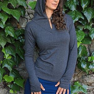 May include: A charcoal gray hooded sweatshirt with a long sleeve and thumb holes. The sweatshirt has a V-neck and a small silver pendant necklace.