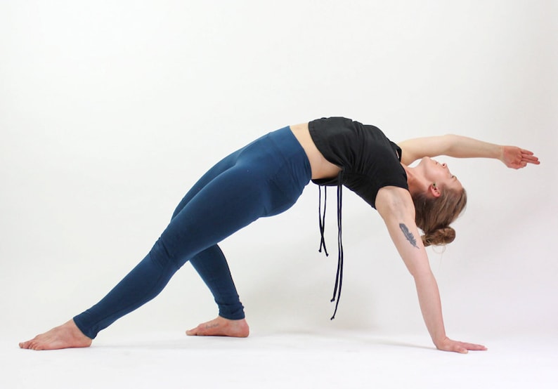May include: A woman in a black crop top and blue leggings performs a yoga pose, bending backwards with her arms extended.