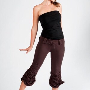 May include: A woman wearing a black strapless top and brown pants with a gathered detail at the bottom. The pants have a belt and a drawstring.
