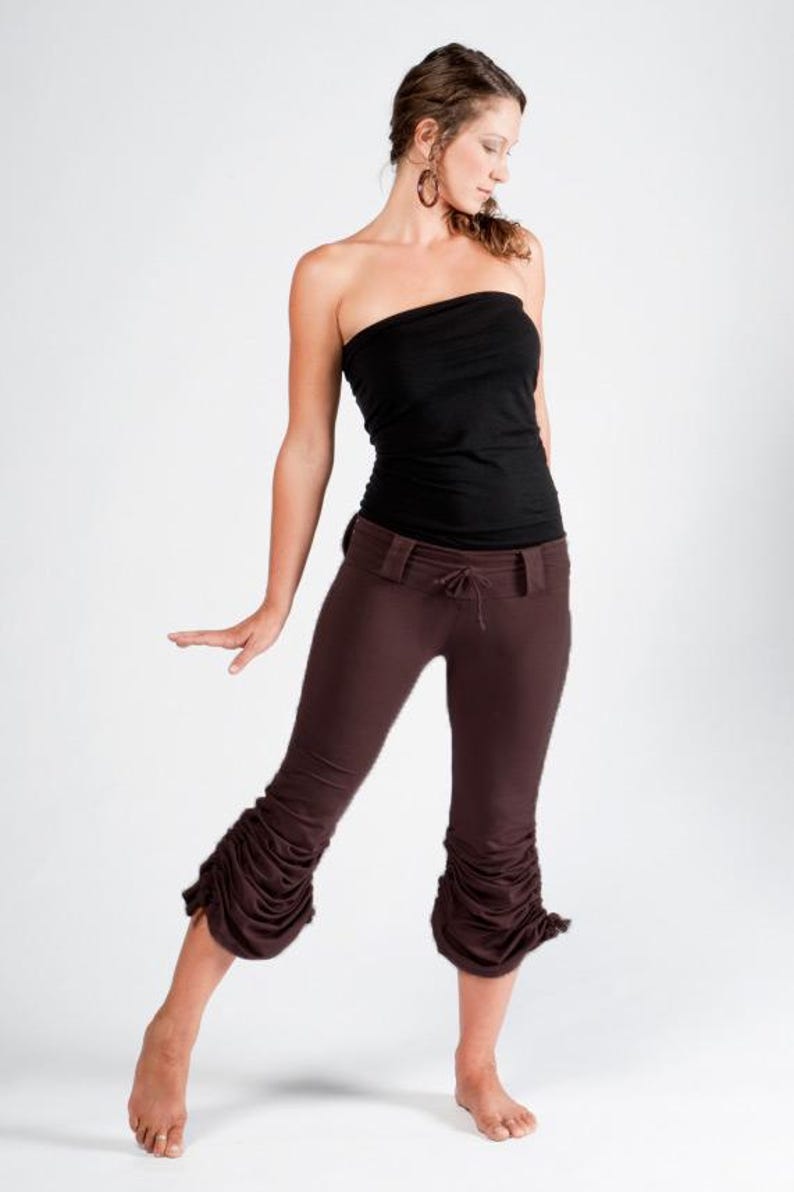 May include: A woman wearing a black strapless top and brown pants with a gathered detail at the bottom. The pants have a belt and a drawstring.