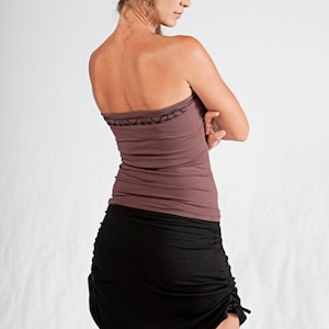 May include: A woman wearing a brown strapless top and a black skirt with a drawstring detail. The skirt is gathered at the front and has a loose fit.