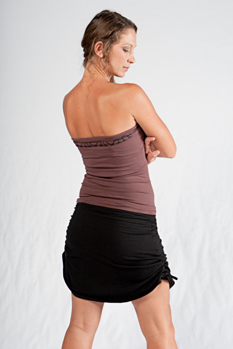 May include: A woman wearing a brown strapless top and a black skirt with a drawstring detail. The skirt is gathered at the front and has a loose fit.