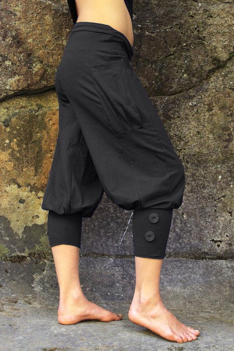 May include: Black cropped pants with a loose, gathered fit and a button detail at the bottom of the legs. The pants have a large pocket on the left side.