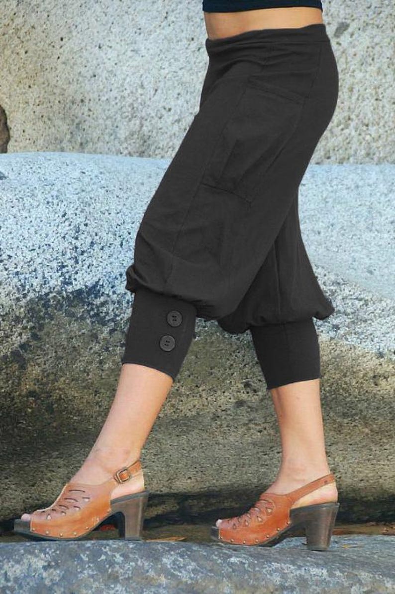 May include: A pair of black cropped pants with a button detail on the leg. The pants are made of a soft, comfortable fabric and have a relaxed fit. The model is wearing the pants with brown sandals.