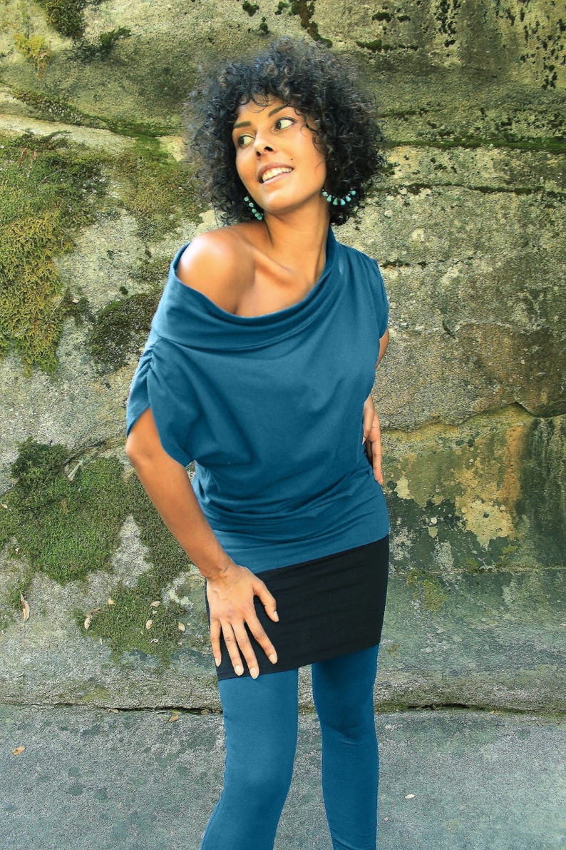 May include: A woman wearing a teal blue off-the-shoulder top with a black skirt and teal blue leggings.