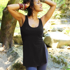 May include: A woman with curly dark hair wearing a black tank top with a side slit and dark blue leggings. She is wearing multiple bracelets on her wrist and a large hoop earring.