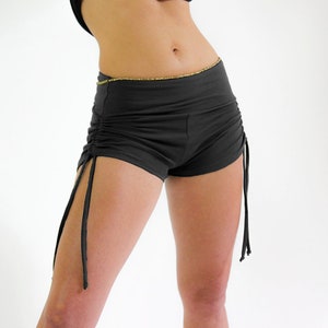 May include: Black shorts with a drawstring detail on the sides. The shorts have a gold trim around the waistband.