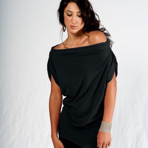 May include: A woman wearing a black off-the-shoulder top with a loose fit and long sleeves. She is wearing black pants and a silver bracelet on her right wrist.