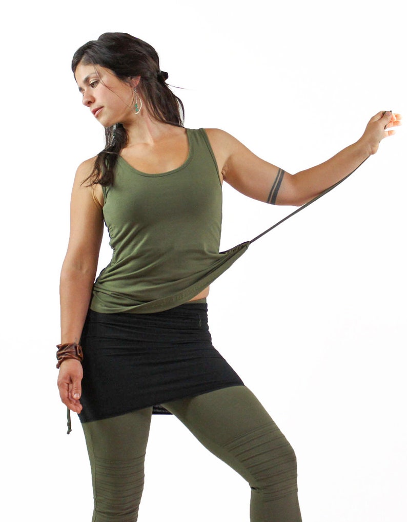 May include: A woman wearing a green tank top with a black skirt and green leggings. The tank top has a tie at the bottom and the skirt is a wrap style.