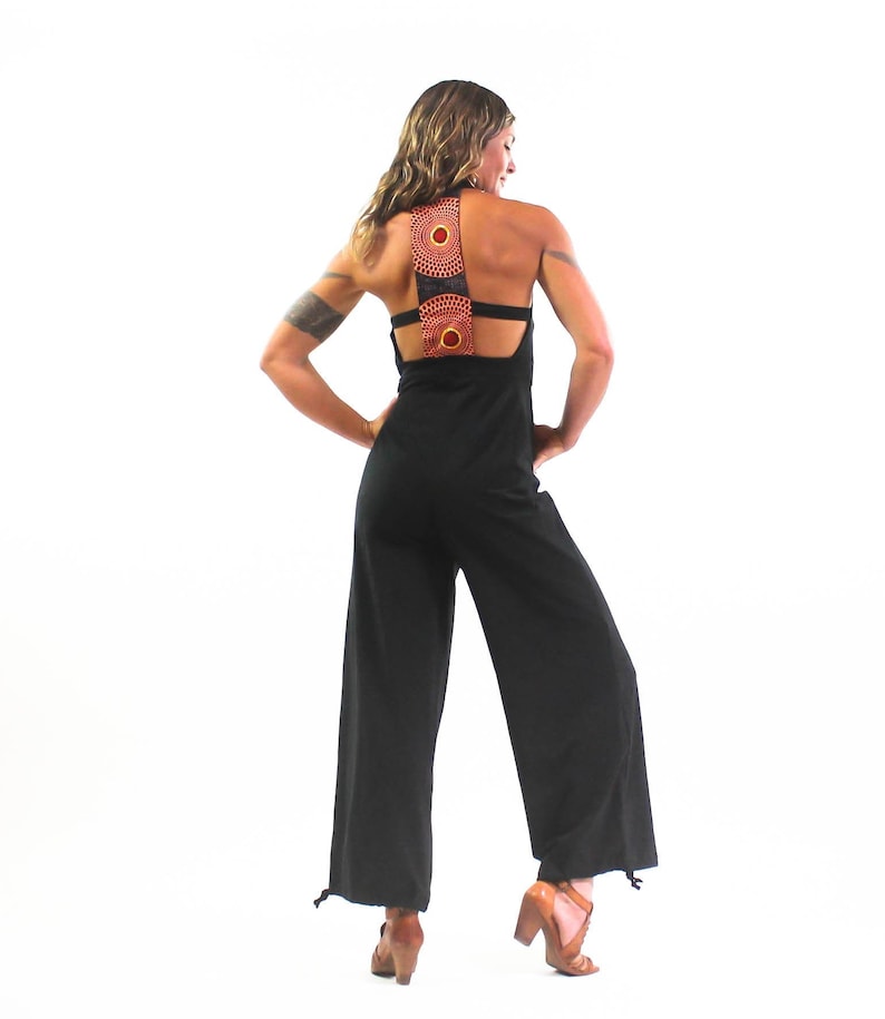 May include: A black jumpsuit with a wide-leg silhouette and a unique back design featuring two circular cutouts with orange and red patterned fabric.