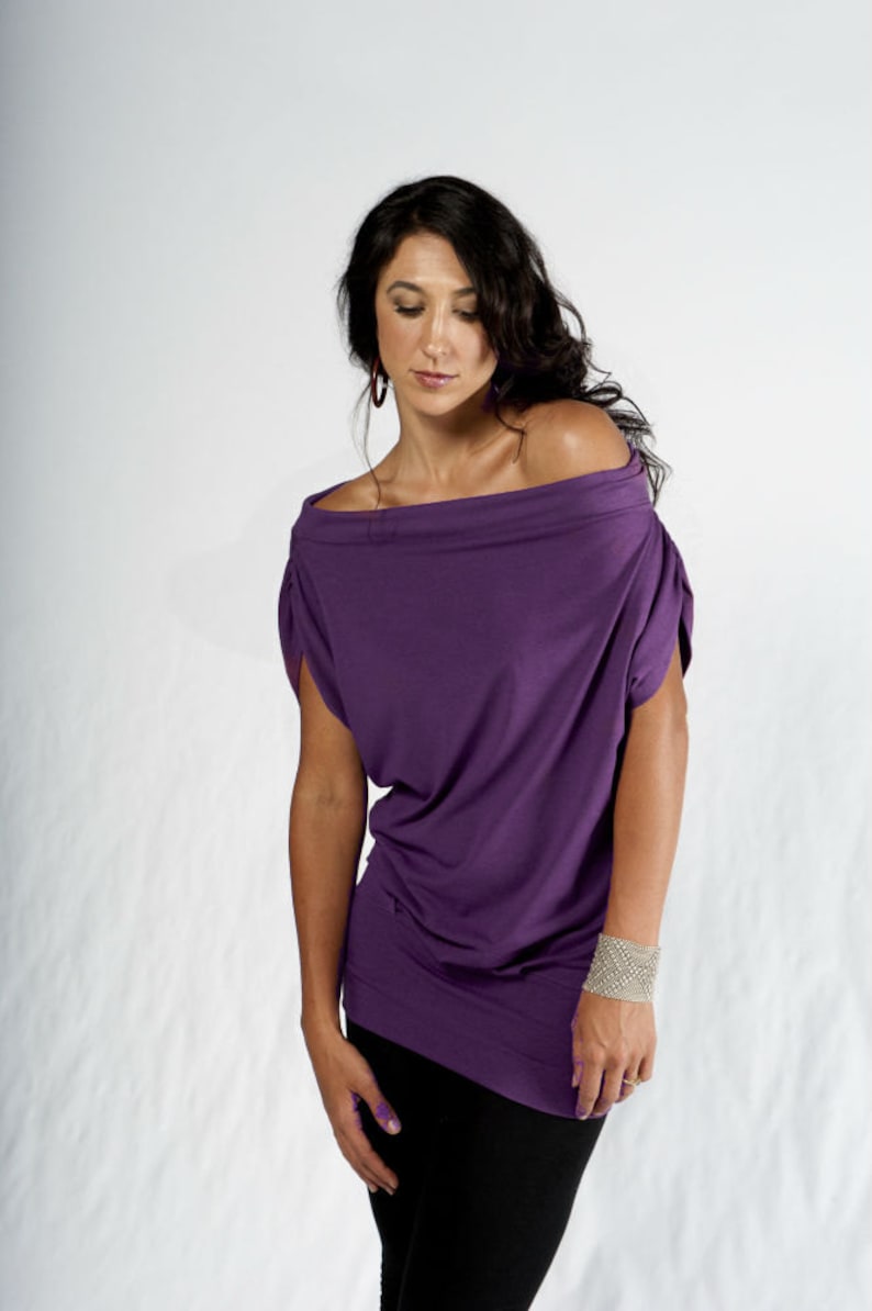 May include: A woman wearing a purple off-the-shoulder top with short sleeves and black pants.