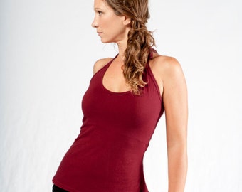 May include: A woman wearing a maroon halter top and a black skirt. She is standing with her back to the camera and looking to the side.