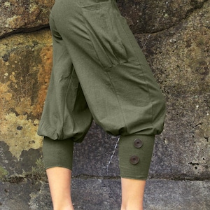 May include: Olive green cropped pants with a relaxed fit. The pants feature a wide waistband, pockets, and gathered cuffs with two decorative buttons. The fabric appears to be a soft, breathable material.