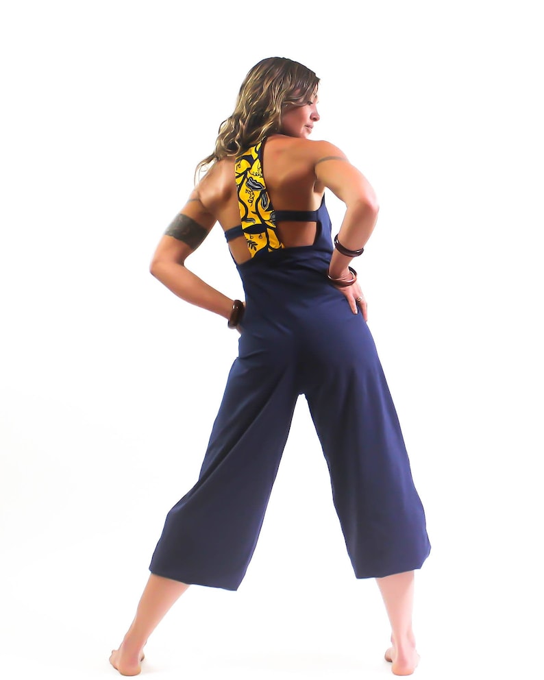 May include: A navy blue jumpsuit with a yellow and black patterned fabric detail on the back. The jumpsuit has a wide leg and a relaxed fit.