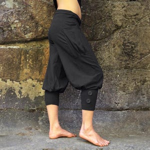 May include: Black cropped pants with a loose, baggy fit and button detailing at the cuffs.