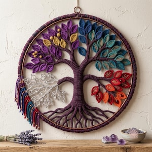 Könnte beinhalten: Ein kreisförmiger Wandbehang mit einem gehäkelten Lebensbaum in einem umwickelten Reifen. Der Baum hat vier verschiedene Blattbereiche in Lila und Gold, Blau und Türkis, Rot und Orange sowie Silber. Eine Franse aus Garn und Perlen hängt an einer Seite.