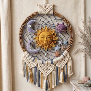 Op de afbeelding: Een ronde macramé wandhanger met een gevlochten wilgenring en een blauw koordweb. In het midden bevindt zich een gehaakte gele zon, geflankeerd door twee paarse maansikkels, een paarse planeet en diverse kleine gehaakte sterren in blauw en beige.