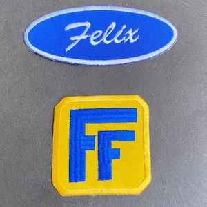 May include: Two embroidered patches. The top patch is an oval shape with a blue background, a white border, and the white script text Felix. The bottom patch is a yellow square with clipped corners, featuring two blue letter Fs in the center.