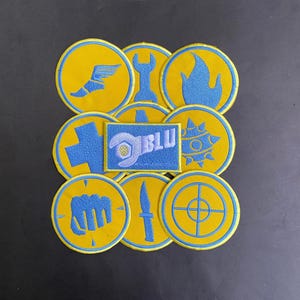 May include: A collection of embroidered patches featuring yellow circular designs with light blue icons including a winged boot, wrench, flame, cross, spiked ball, fist, knife, and target, plus a rectangular blue patch with the text BLU.