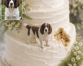 May include: A three-tiered white frosted cake featuring a small, detailed figurine of a brown and white English Springer Spaniel standing on the middle tier. The cake is decorated with small white flowers and green foliage accents.