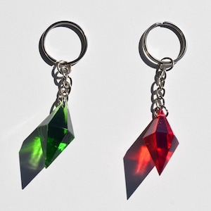 Può includere: Due portachiavi con ciondoli sfaccettati a forma di diamante realizzati in materiale traslucido. Un ciondolo è verde scuro e l'altro è rosso brillante. Ognuno è fissato a una catena in metallo argentato e a un anello circolare per chiavi.