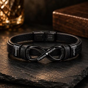 Peut inclure: Un bracelet en cuir noir doté d'un symbole infini central en métal noir poli. Les éléments métalliques sont gravés avec les noms Elowen, Graeme, Mariza et Zephyr, avec un symbole de cœur entre Graeme et Mariza.