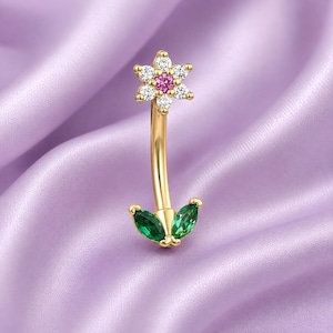 May include: A gold curved barbell body jewelry piece featuring a flower-shaped top with six clear white stones surrounding a central pink stone, and a bottom accent consisting of two marquise-cut green stones arranged to resemble leaves.