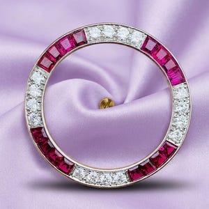 May include: A circular brooch featuring alternating sections of square-cut red rubies and round brilliant-cut white diamonds set in a metallic frame. The design consists of four segments of rubies and four segments of diamonds arranged in a ring.