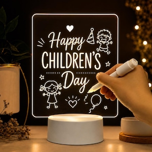 Może przedstawiać: Prostokątna tablica akrylowa z białą, podświetlaną podstawą. Na tablicy znajduje się napis Happy CHILDREN'S Day, serce, czapeczka imprezowa, balon oraz rysunki liniowe dwojga dzieci. Biały marker jest używany do rysowania na powierzchni tablicy.