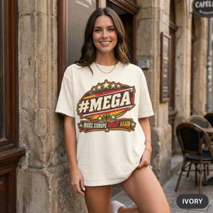 Smiling woman in front of a café in an old town wearing the "#MEGA Make Europe Great Again" Germany T-shirt by SarcasmArt in Ivory.