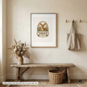Pode incluir: Uma impressão artística emoldurada com a ilustração de um cervo dentro de uma borda oval com o texto PLEASE DO NOT APPROACH. A impressão é exibida em uma moldura de cor clara de 40 por 50 cm, pendurada em uma parede bege.
