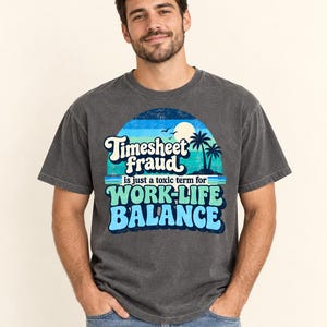 Smiling man wearing the "Timesheet Fraud Is Just a Toxic Term for Work-Life Balance" sarcastic work T-shirt by SarcasmArt in Pepper (washed charcoal), showing the retro sunset work-life balance print.