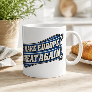 Scotland Mug – Make Europe Great Again Coffee Cup by SarcasmArt. A white ceramic mug featuring a blue and black graphic design with the text "MAKE EUROPE GREAT AGAIN" enclosed within a stylized banner shape, accented by small stars on the left and right sides of the text block.