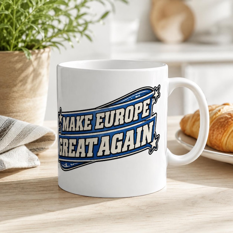 Scotland Mug – Make Europe Great Again Coffee Cup by SarcasmArt. A white ceramic mug featuring a blue and black graphic design with the text "MAKE EUROPE GREAT AGAIN" enclosed within a stylized banner shape, accented by small stars on the left and right sides of the text block.
