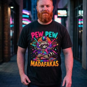 Bearded man on a neon-lit city street at night wearing the "Pew Pew Madafakas" raccoon meme T-shirt by SarcasmArt in Black.