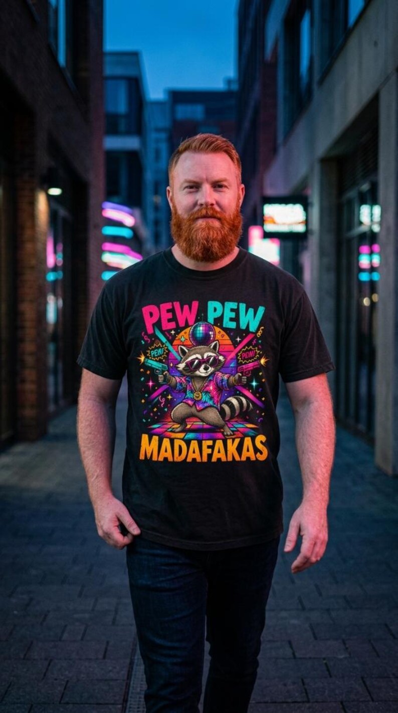 Bearded man on a neon-lit city street at night wearing the "Pew Pew Madafakas" raccoon meme T-shirt by SarcasmArt in Black.