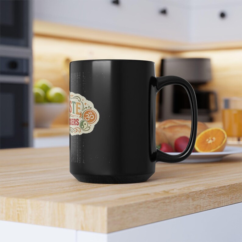 Side view of the black "Namaste Motherfuckers" funny yoga coffee mug by SarcasmArt on a kitchen counter with fruit.