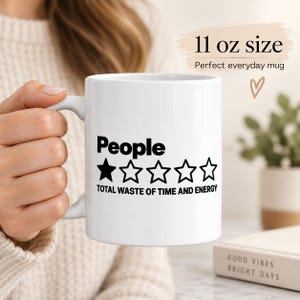 11 oz size: a woman in a cozy sweater holding the "People – 1 Star, Total Waste of Time and Energy" sarcastic coffee mug by SarcasmArt – a perfect everyday mug.